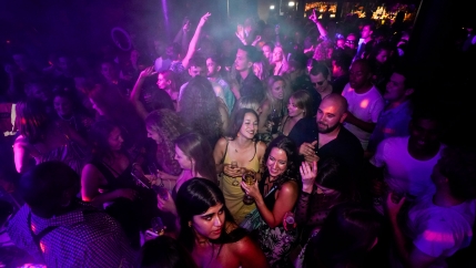 A crowded dance floor is shown in London with people dancing under purple and pink lighting.