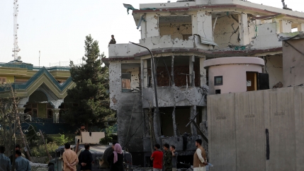 People stand around a bombed-out building