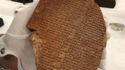 White-gloved hand holds ancient artifact known as the Gilgamesh Dream Tablet. 