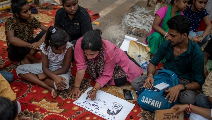 A woman surrounded by other people writes on a white placard