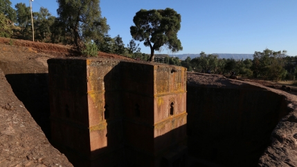 An several storeys tall stone church is shown carved into the side of a hillside.