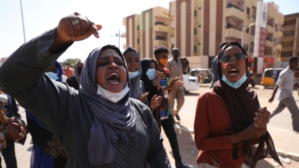 Two women are shown at the head of a group of protesters, one with her hand rised in the air.