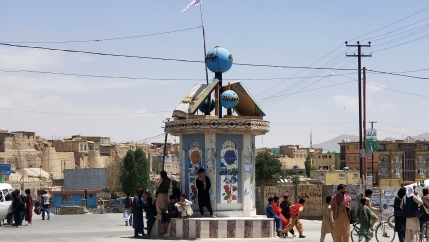 Several people are shown sitting and standing around the center, circular post in the open air city square.