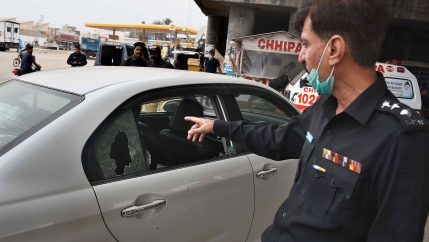 A police officer examines a damaged car at the site of a firing incident, in Karachi, Pakistan