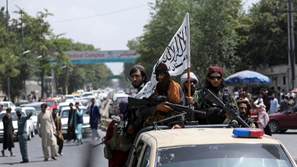 A group of heavily armed bearded men are shown riding in the back of a police pickup truck.