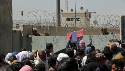 A larger crowd of people are shown crammed up against large cement barriers with barbed-wire on top.