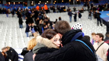 A man is shown hugging a woman who is looking into the camera with empty stadium seats in the distance.
