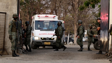 A white ambulance is shown from the front with several people wearing military fatigues and carrying weapons standing nearby.
