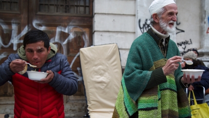 Chilean Muslims and people from other religious communities eating a meal from bowls, outside at the weekly soup kitchen in Santiago, Chile.