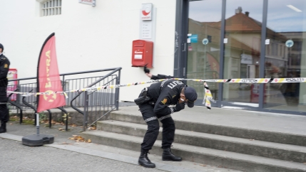 A police officer is shown bending down to walk under yellow caution tape outside of a set of glass doors.