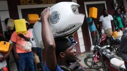 A man balances his motorbike tank on his head as he waits outside a gas station in hopes of filling his tank, in Port-au-Prince, Haiti, on Oct. 23, 2021. The ongoing fuel shortage has worsened, with demonstrators blocking roads and burning tires in Haiti'