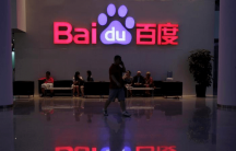 An employee uses his mobile phone as he walks past the company logo of Baidu at its headquarters in Beijing, Aug. 5, 2010.