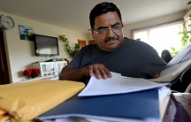 Man sits behind large stack of papers, brown envelopes