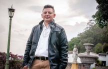 A man wearing a leather coat stands in a public square.