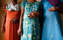 Three women stand in a line with their hands on their visibly pregnant stomachs. Their faces are cropped out of the image.