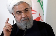 Iran President Hassan Rouhani with his right hand raised and finger pointed upward.
