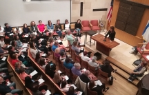 Overhead view of congregation in pews, while woman stands at podium speaking