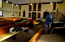 Jewish man prays at altar with pews behind him, USA flag in background