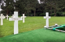 Two white crosses engraved with names sit in a cemetary