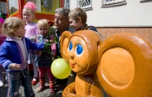 A man poses with small children next to a wooden image of the cartoon character Chebrashka.