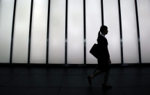 A woman in a business suit is silhouetted against a bright building
