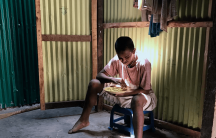 a young Rohingya man with intellectural disabilities sits in his makeshift home