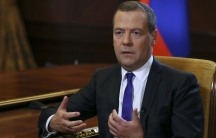 Russian Prime Minister Dmitry Medvedev is shown sitting in a chair with yellow fabric, speaking during an interview outside Moscow.