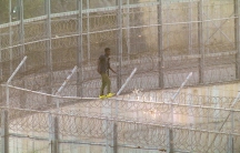 an african migrant scales a razor-wire topped fence in Ceuta, Spain