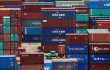 Shipping containers are seen at a port in Shanghai, China, with a green truck driving through the middle.
