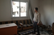 man looking out a broken window, surrounded by rubble