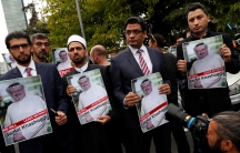 Four men wearing suits stand abreast holding posters of Saudi journalist Jamal Khashoggi's picture.