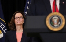 CIA Director Gina Haspel stands behind President Donald Trump with the Agency and US flags behind her.