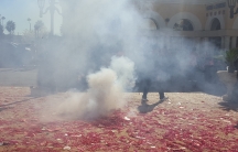 Smoke in front of a man, with remnants of firecrackers on the ground