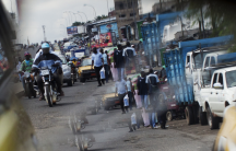 A reflection from the wing mirror of a car shows people ride motorcycles in Douala.