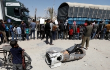 A boy stands next to the remains of a missile as people line up for aid in the city of Douma in Damascus, Syria, on April 16, 2018.