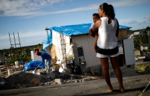 a woman holds a child in front of destroyed building