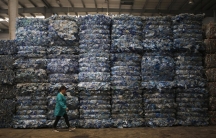 A worker walks past piles of plastic PET bottles at Asia's largest PET plastic recycling factory