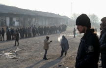 Migrants stand in line to receive free food outside a derelict customs warehouse in Belgrade