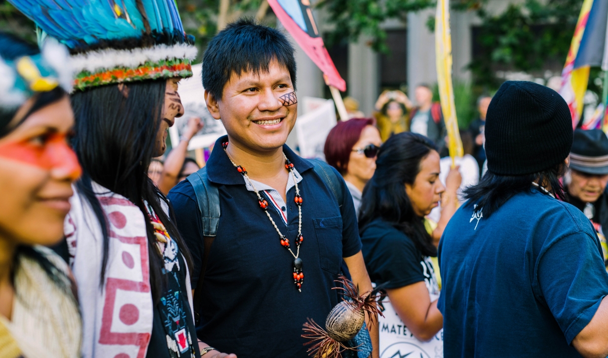 Leo Cerda is shown, adorned with indigenous wears in a crowd of activists in San Francisco.
