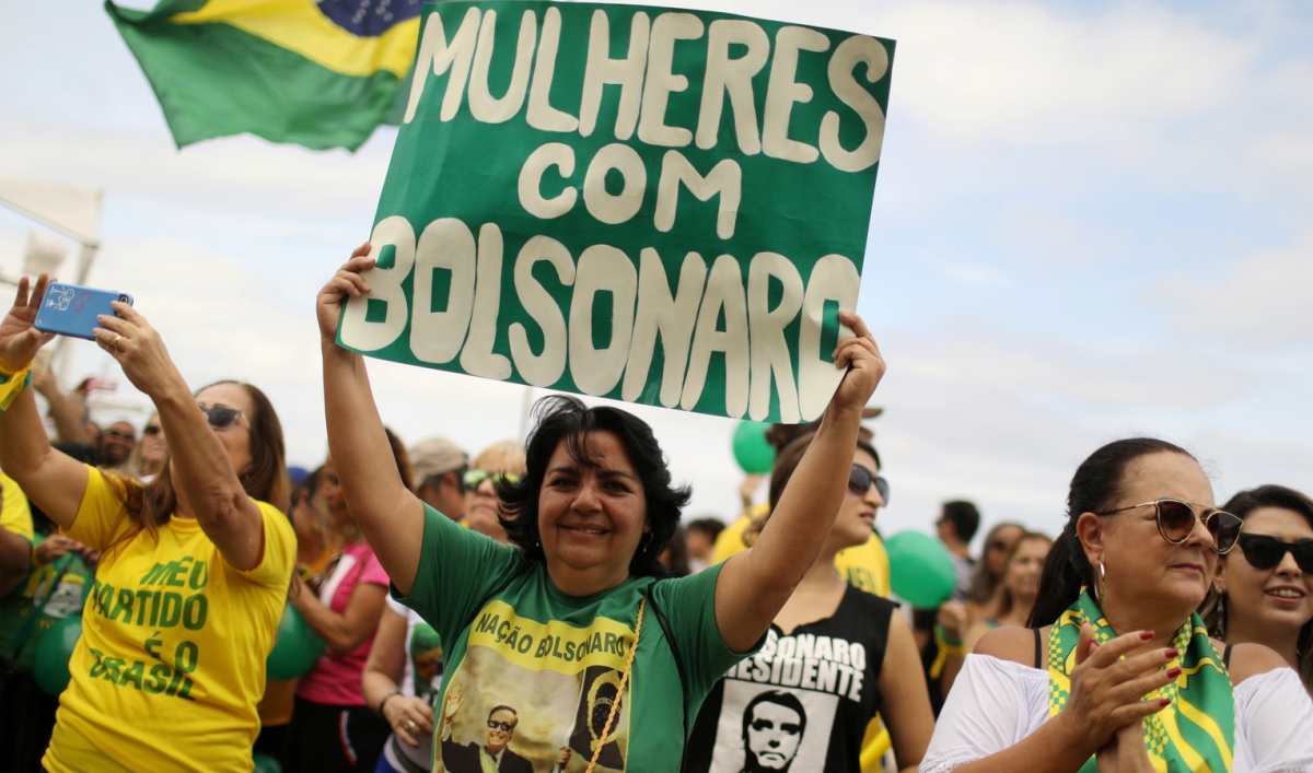 A woman holds up a green sign with white letters that says "Women for Bolsonaro"