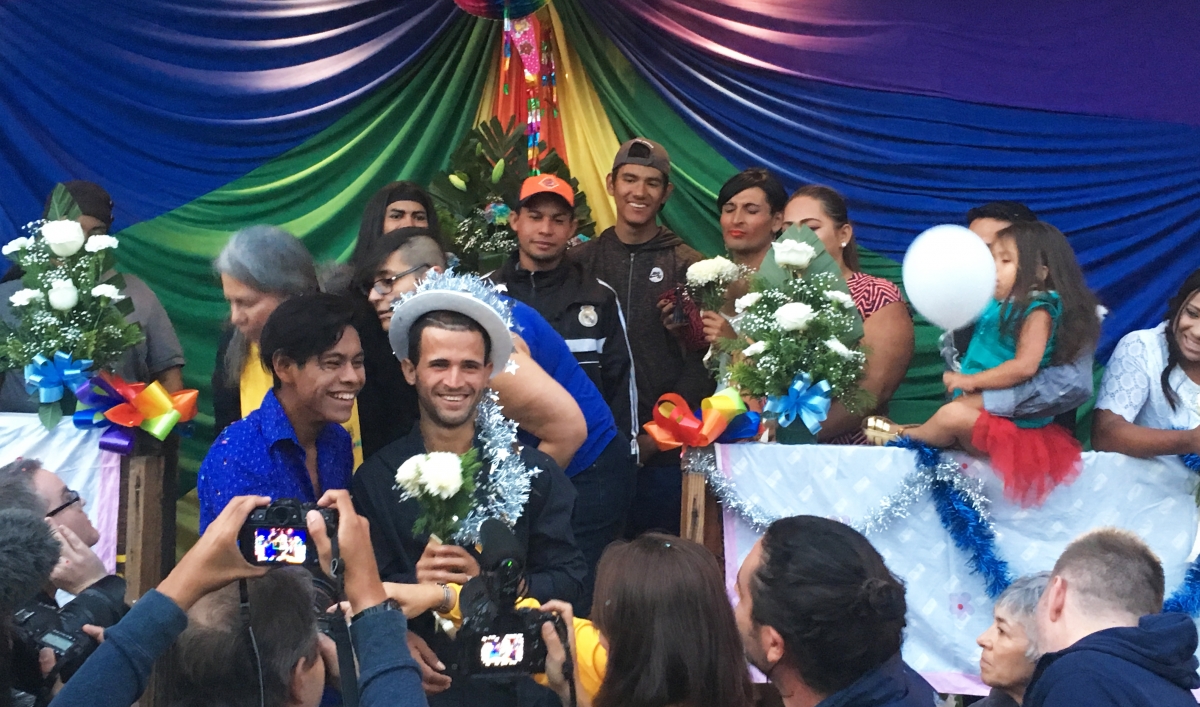 One of seven LGBTQ couples that got married in Tijuana, Mexico pose for a picture with an LGBTQ rainbow flag behind them