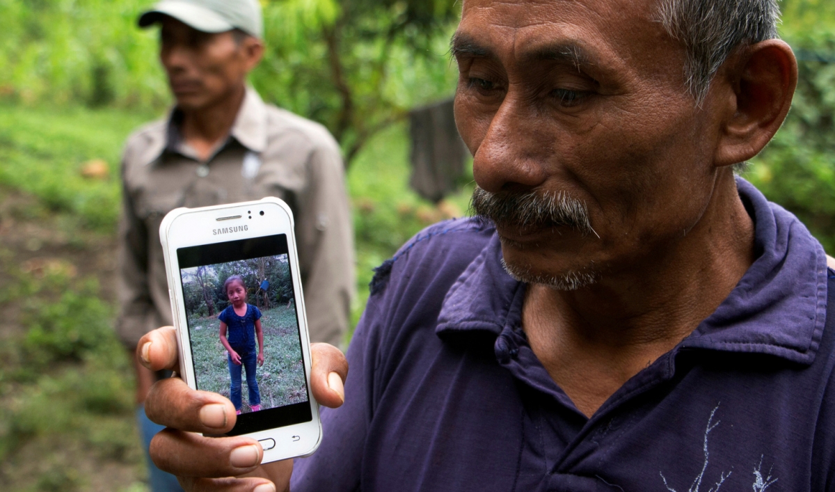 A man holds a phone with a picture of his granddaughter.