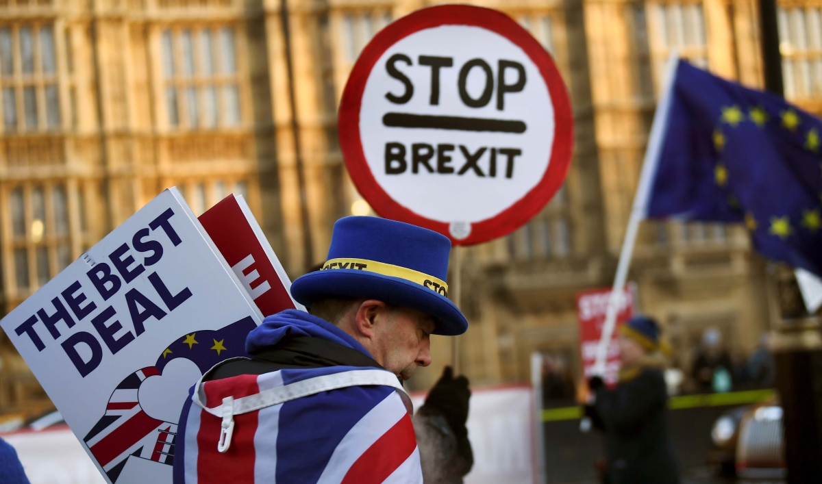 A man with a top hat and UK flag draped around his shoulders holds anti-Brexit protest signs