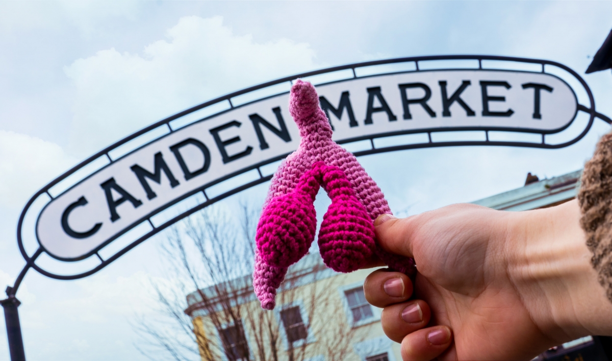 a knitted clitoris is held in front of the Camden Market sign