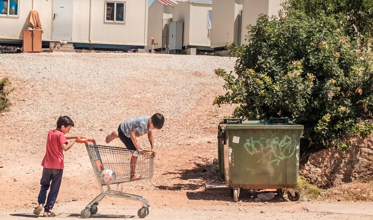 Two young children are shown playing with a grocery cart with container homes shown in the background.