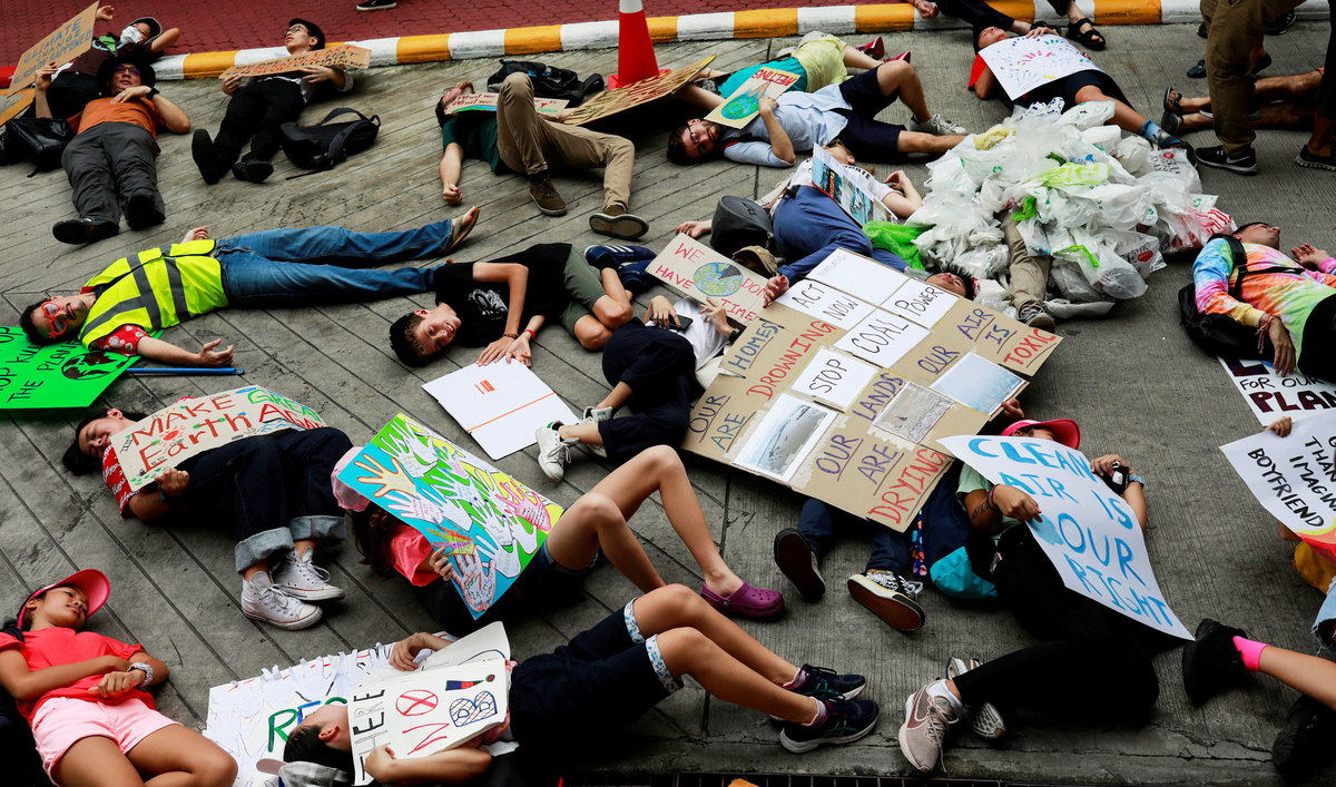 Several young people are shown laying down on the ground with placards protesting for climate change action.