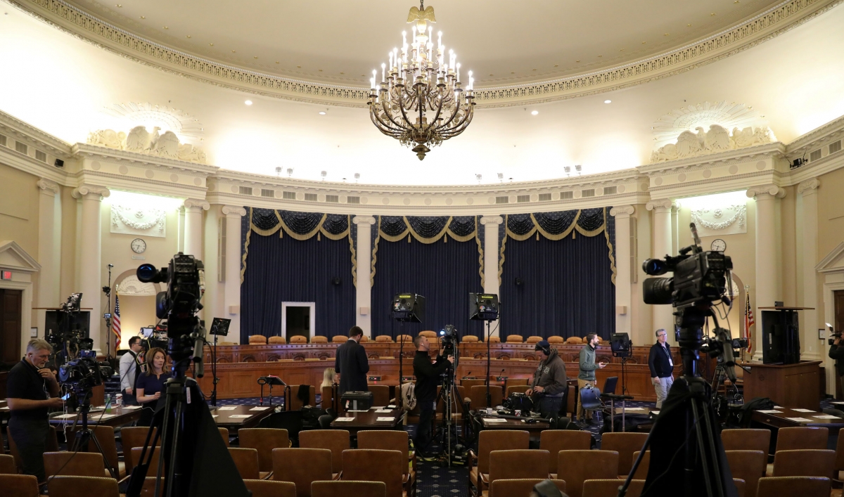 A House committee room is shown with a chandelier hanging from the ceiling and two television cameras placed among the seats.