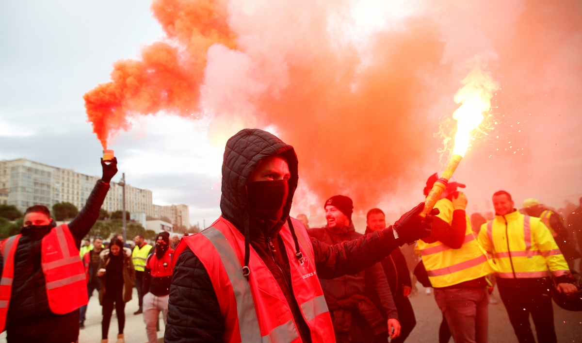 A group of protesters are shown wearing reflective vest and two men are holding bright road flares.
