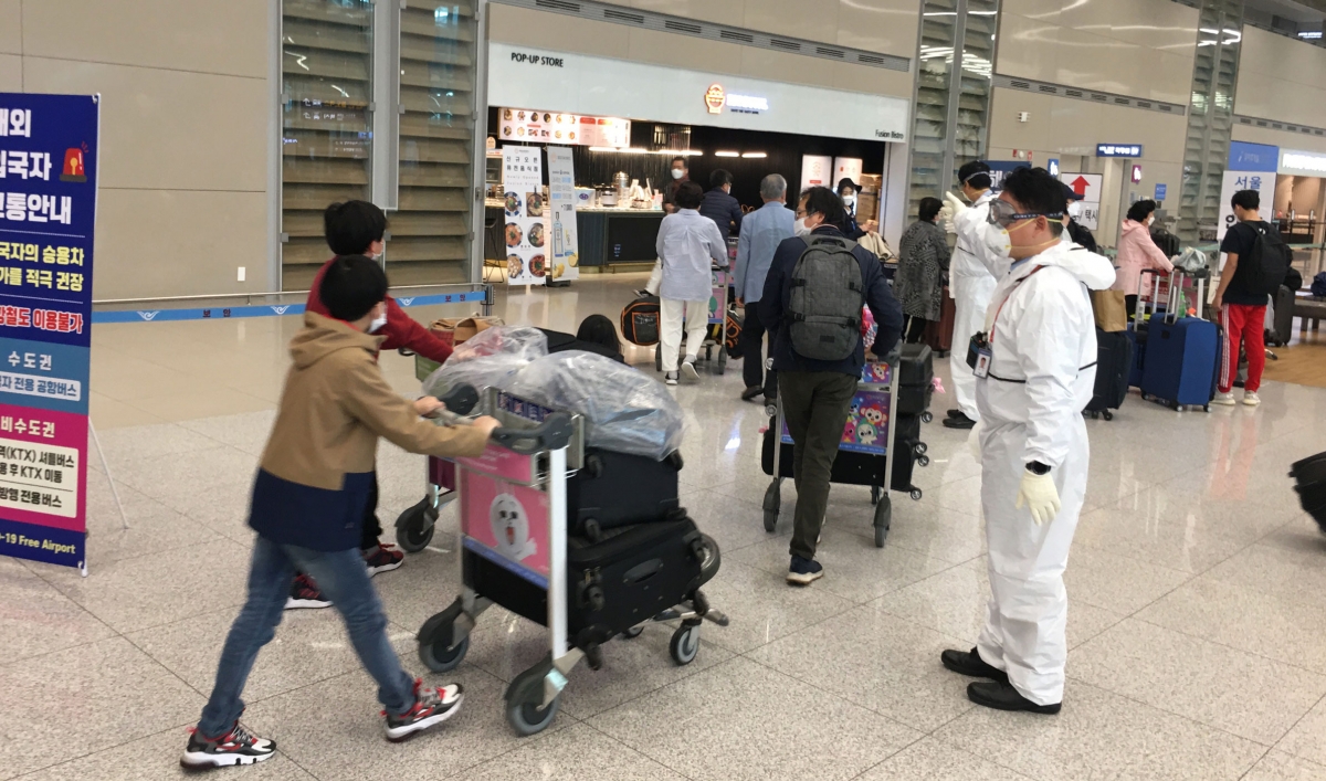 Arrivals at Incheon International Airport are directed by staff in protective gear.