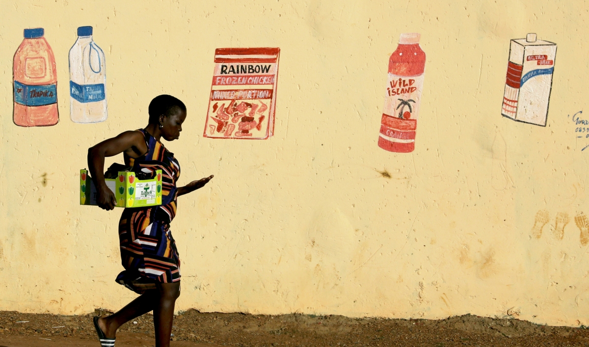 A woman walks home in front of a wall with supermarket mural of grocery items